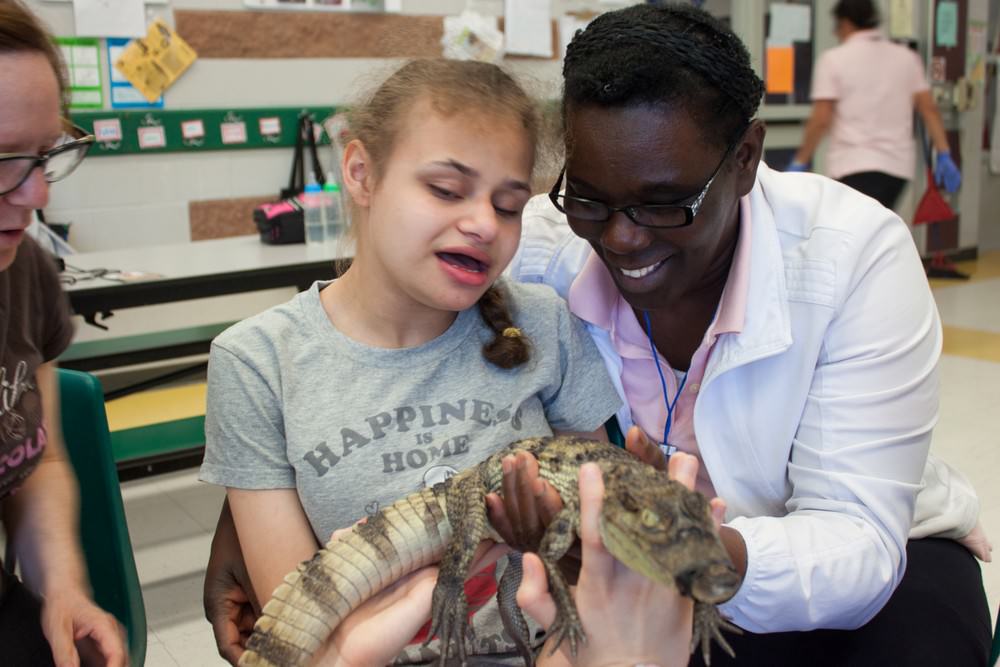 A young girl holding a reptile with a VHA Playdate staff member at a petting zoo event