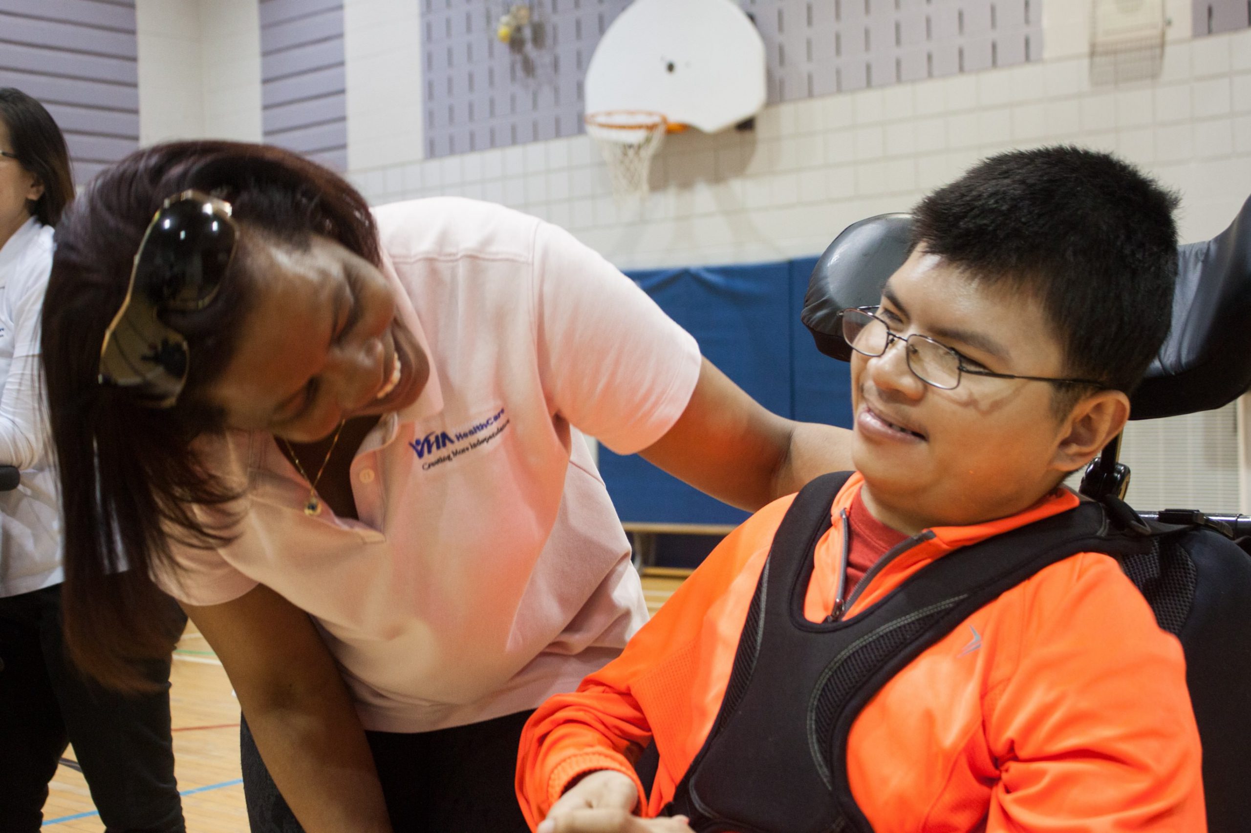 A boy in a wheelchair in a gymnasium with a VHA Playdate staff member smiling at him