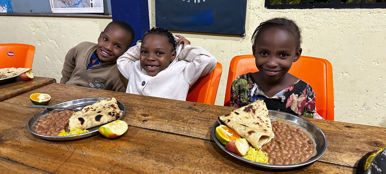 Three young children in Tanzania with two plates of nutritious food in front of them