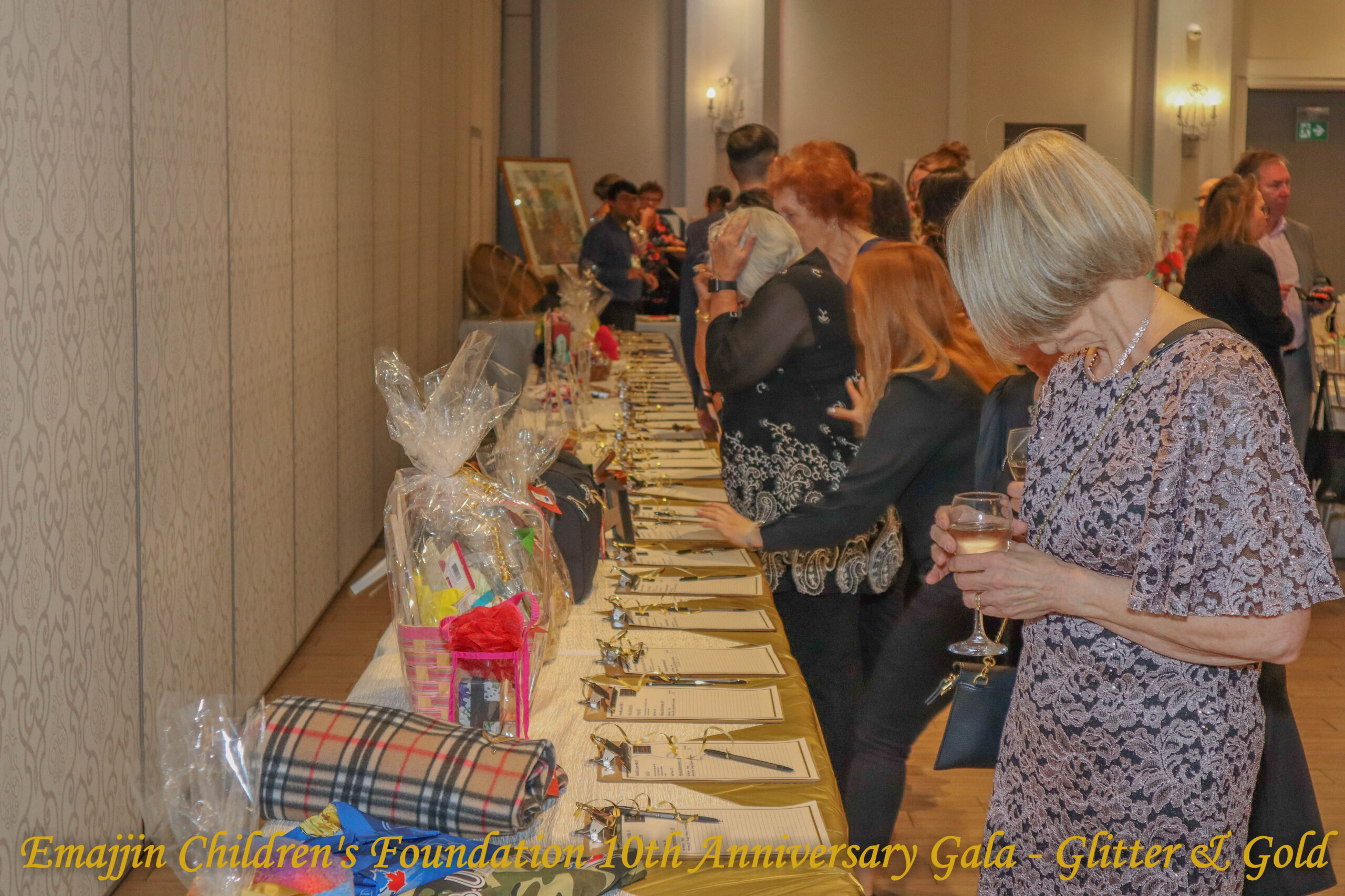 Lady standing in front of the silent auction table browsing among guests at the Emajjin 2024 Gala