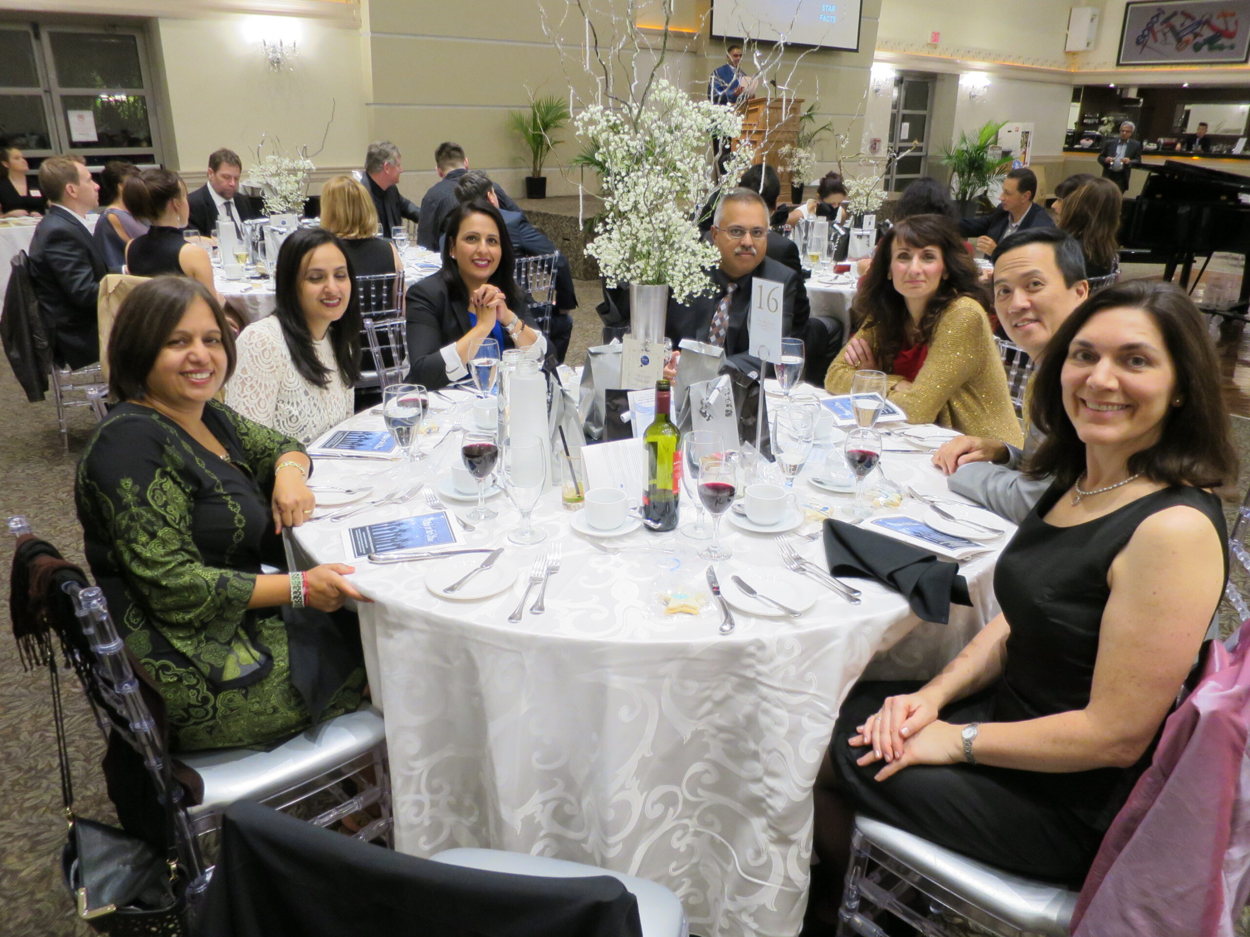 Seven guests seated around a circular table with drinks and a centrepiece at the 2015 Emajjin gala