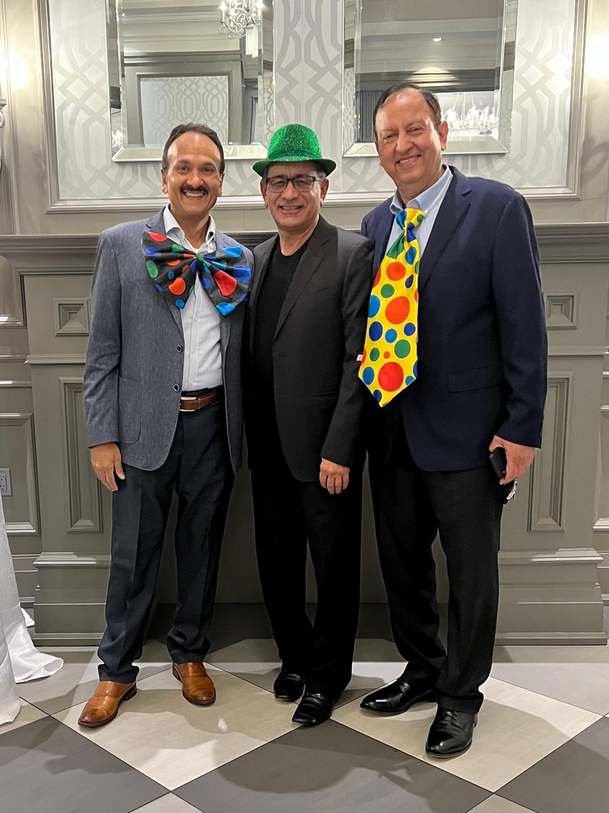 Three men posing and smiling wearing fun props including cartoon ties and hats at the 2022 Celebration gala