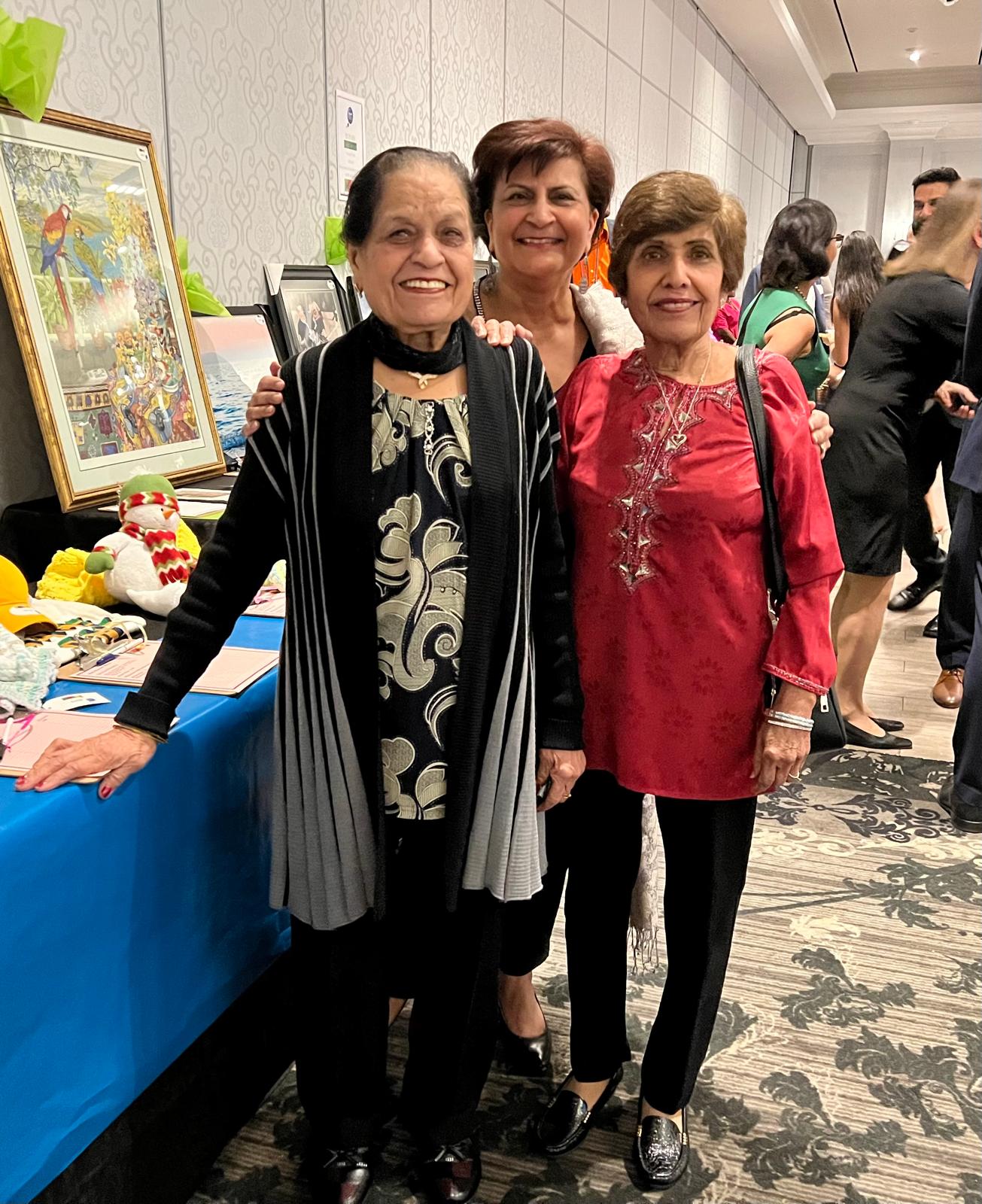 Three ladies smiling at the camera in front of the silent auction table at the 2022 Emajjin Celebration gala